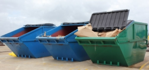 3 large enclosed skips 2 blue and one green) with lids open in skip hire yard